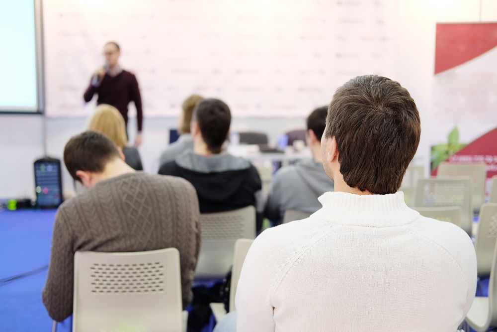 Man looking over people in front of him to see speaker in classroom