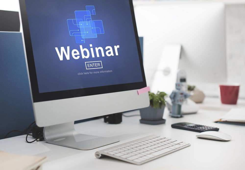Desktop monitor displaying “Webinar” on a bright office desk with keyboard and mouse