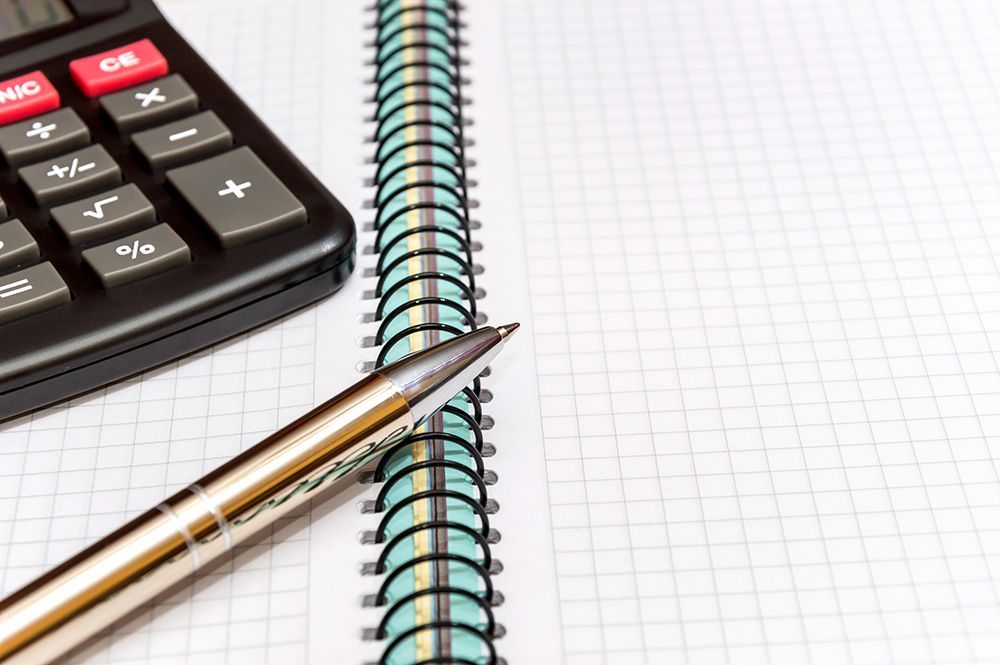 A calculator and a metallic pen resting on the spiral binding of an open grid-lined notebook.