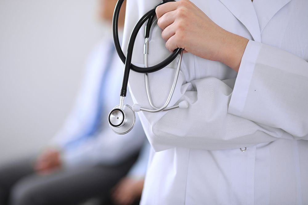 Doctor holding stethoscope standing in front of patient sitting in the background