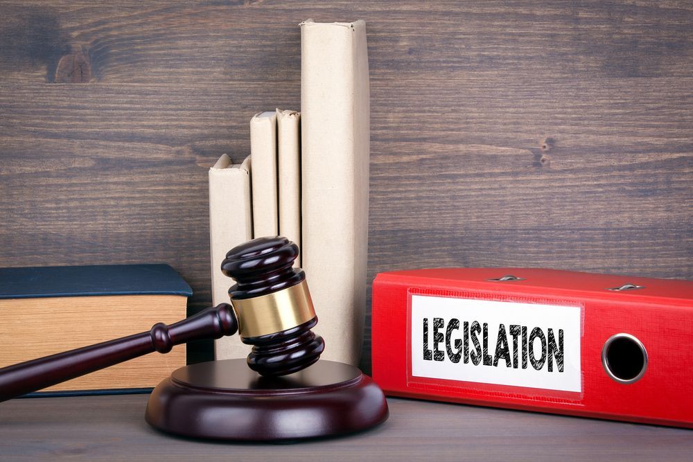 A wooden judge's gavel rests on its block next to several books and a red binder labeled
