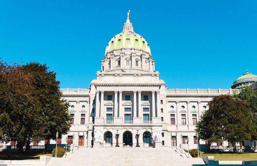 Dome-topped state capitol building with grand steps and columns under a bright blue sky