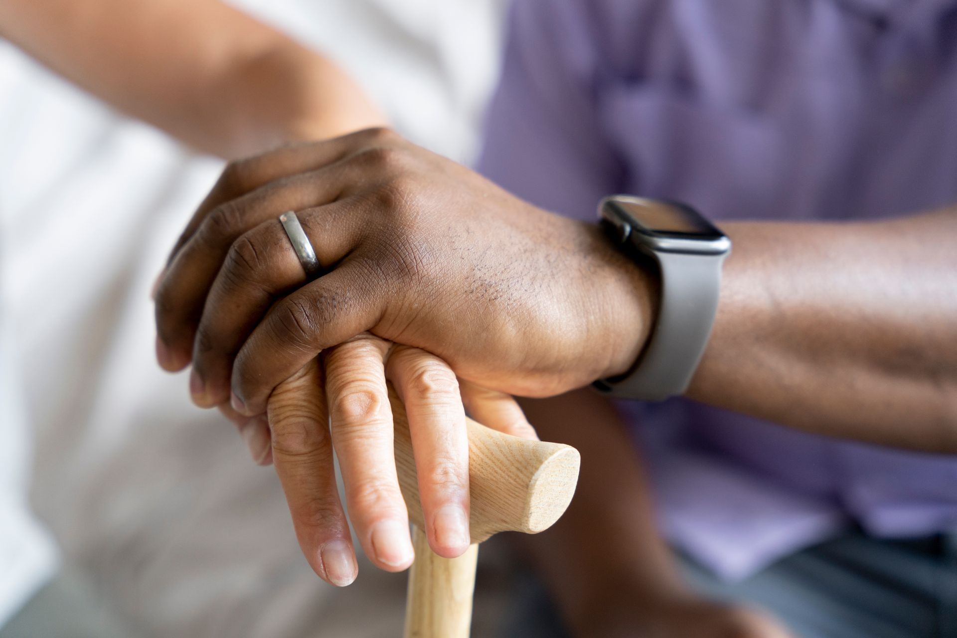 Hands resting on a wooden cane, with one wearing a smartwatch and ring.