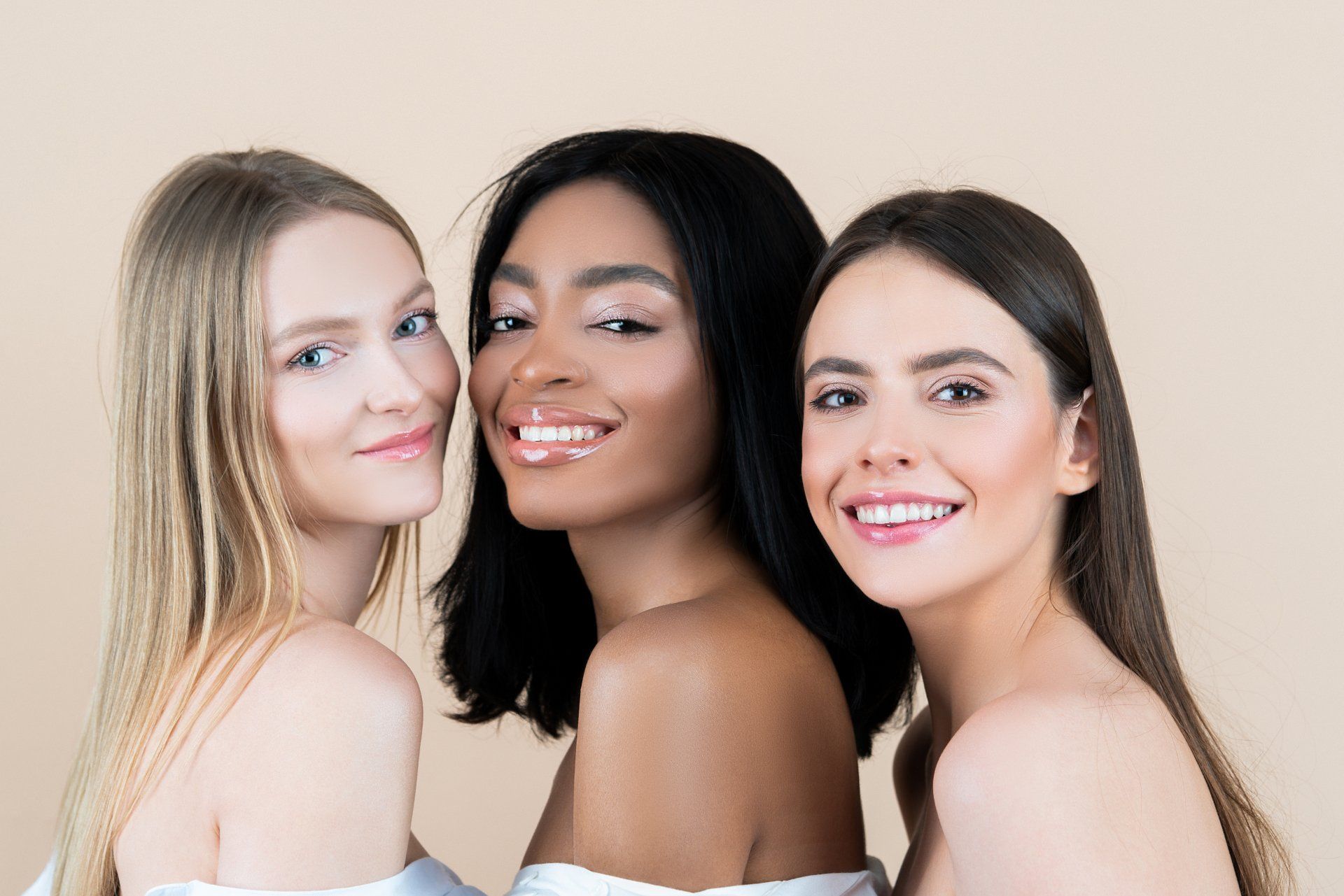 Three women of different races are posing for a picture together and smiling.