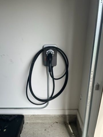 Electric vehicle charger mounted on a white wall in a garage; black cable looped around the charger.