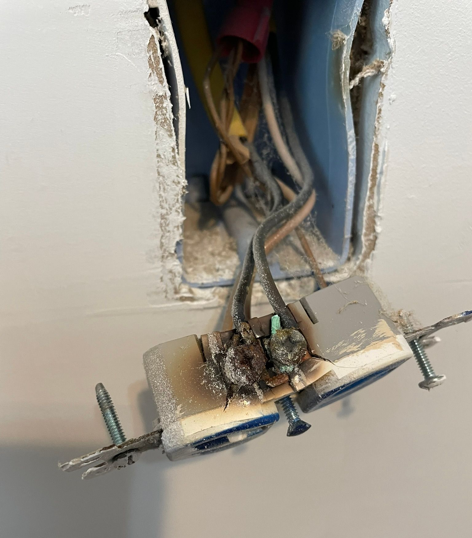 Burnt electrical outlet with exposed wires in a wall. Blackened switch and surrounding damage.