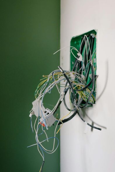 Electrical wires spilling out of a green outlet box on a white and green wall.