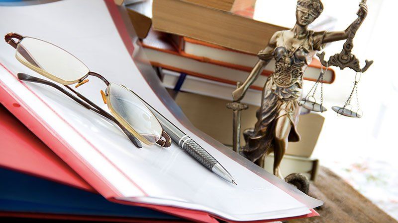 Glasses and a pen on top of paper, with a justice statue in the background