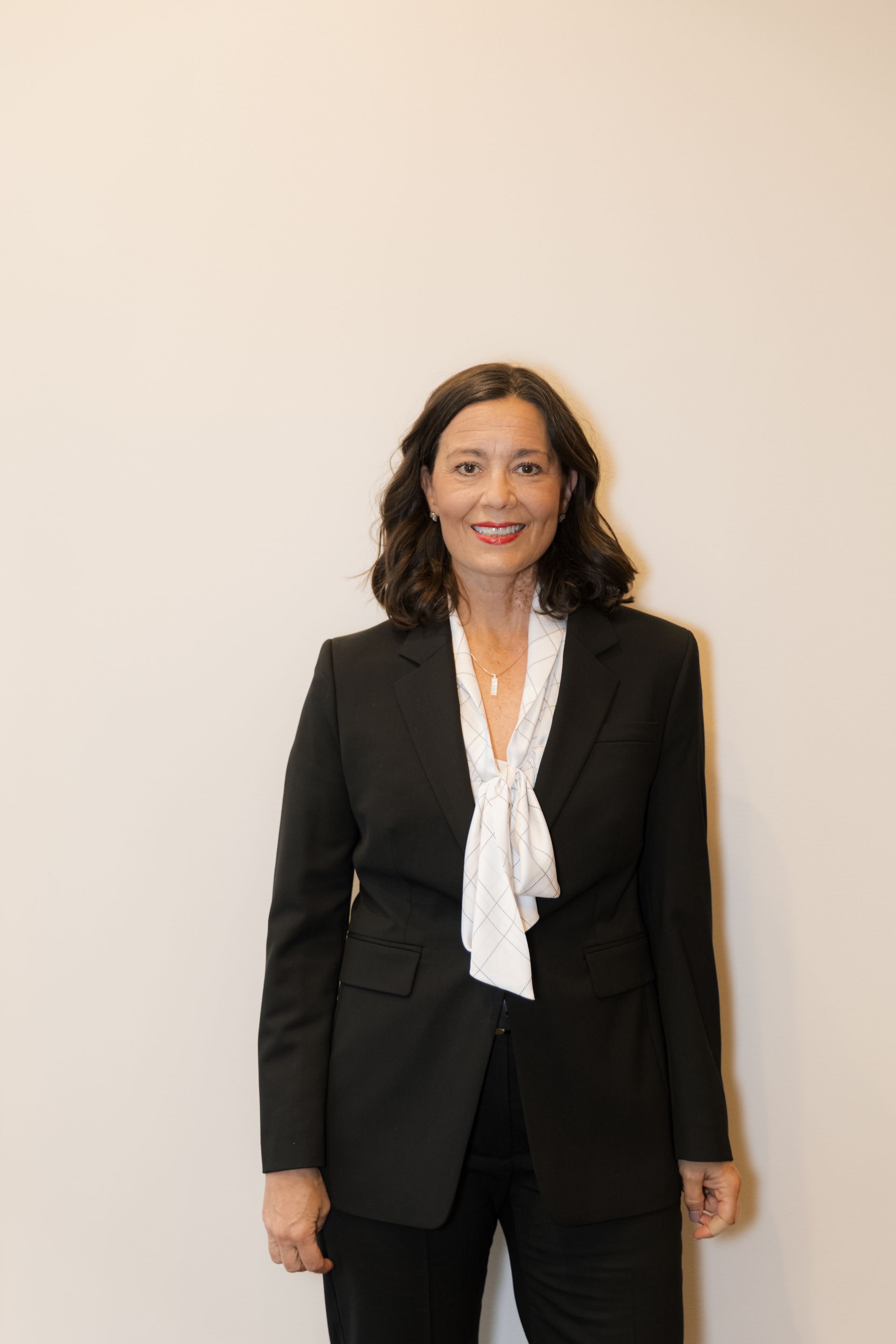 A woman in a suit and tie is standing in front of a white wall.