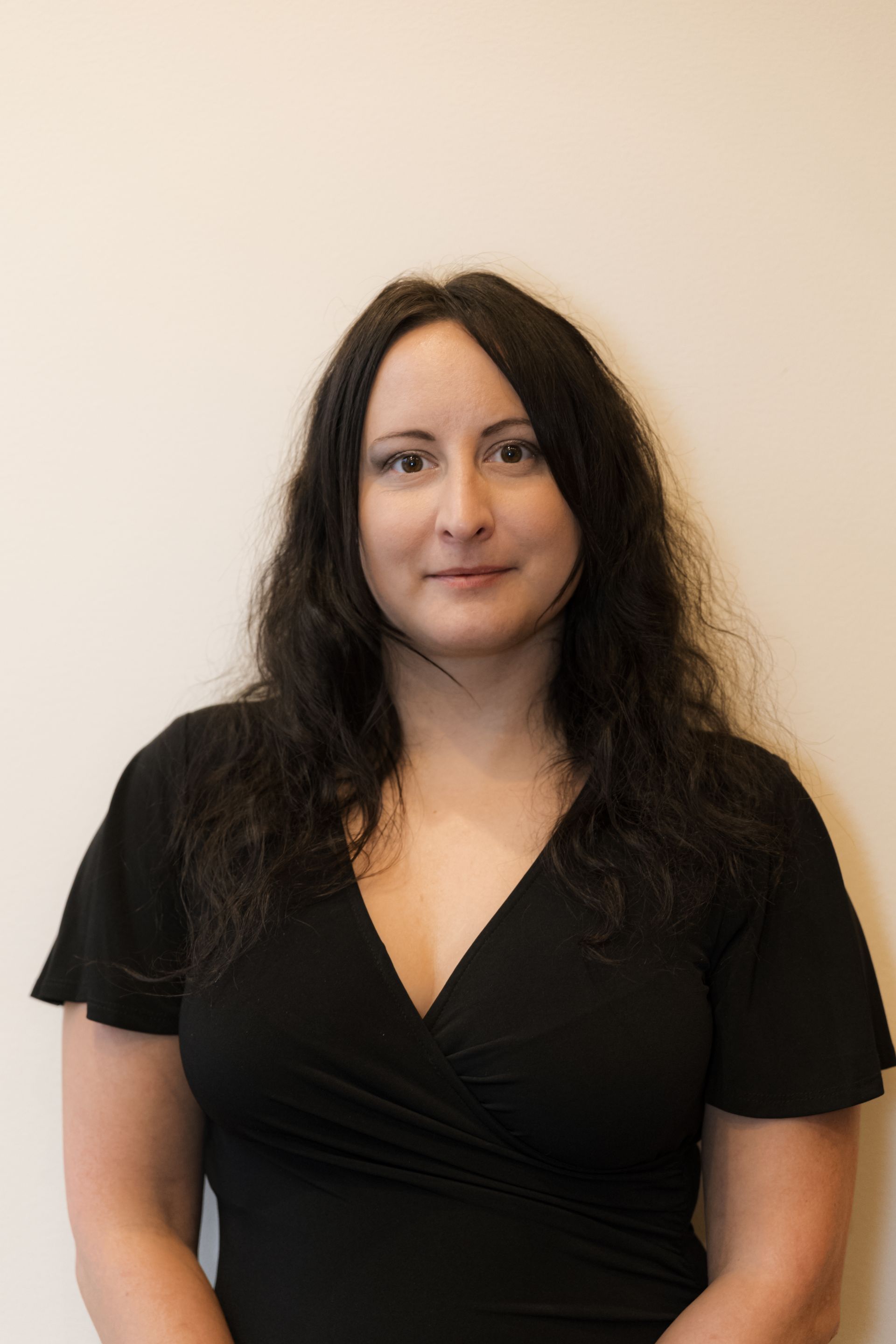 A woman in a black dress is standing in front of a white wall.