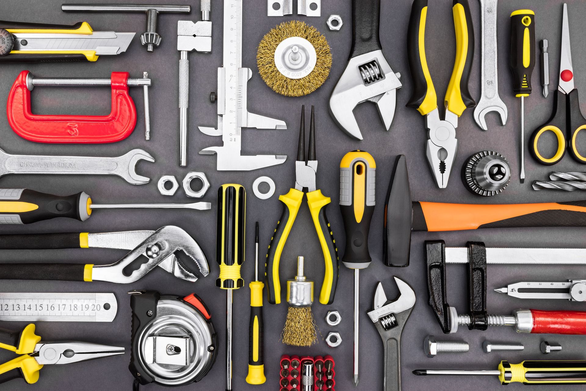 Un assortiment d'outils à main, comprenant des pinces, des clés, un mètre ruban et un serre-joint, disposés sur un fond gris foncé.