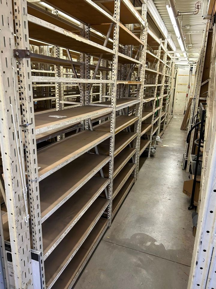 Des rayonnages industriels vides sont alignés le long d'un sol en béton dans une allée d'entrepôt.