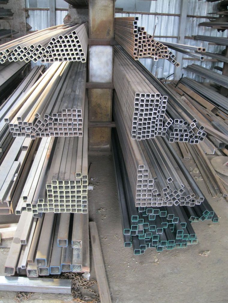 Des piles d'éléments d'échafaudage en métal bleu sont disposées sur un champ herbeux sous un ciel lumineux.