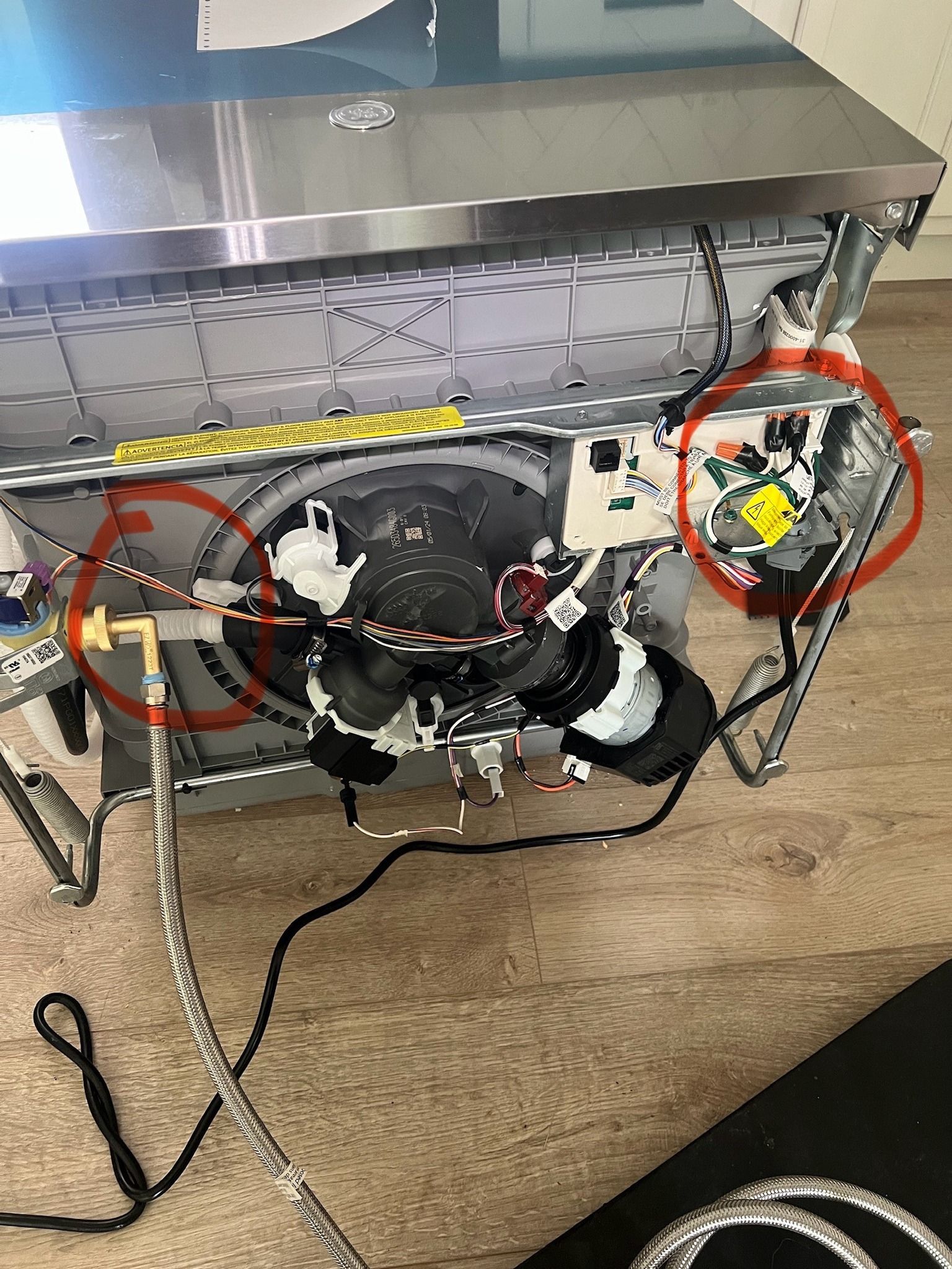 A dishwasher is sitting on a wooden floor with a bunch of wires coming out of it.