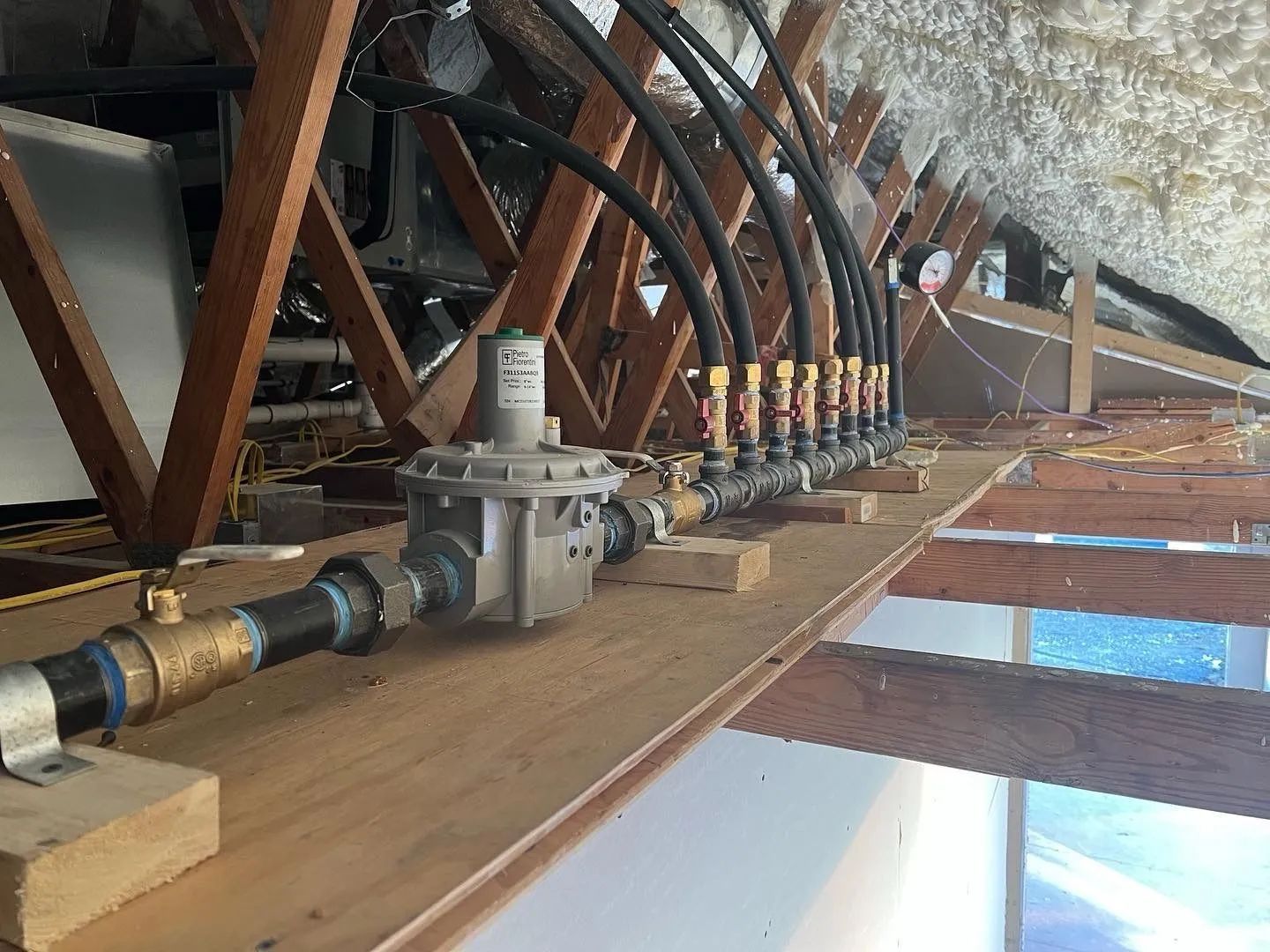 Row of industrial gas regulators and pipes mounted on a wooden platform under a metal roof