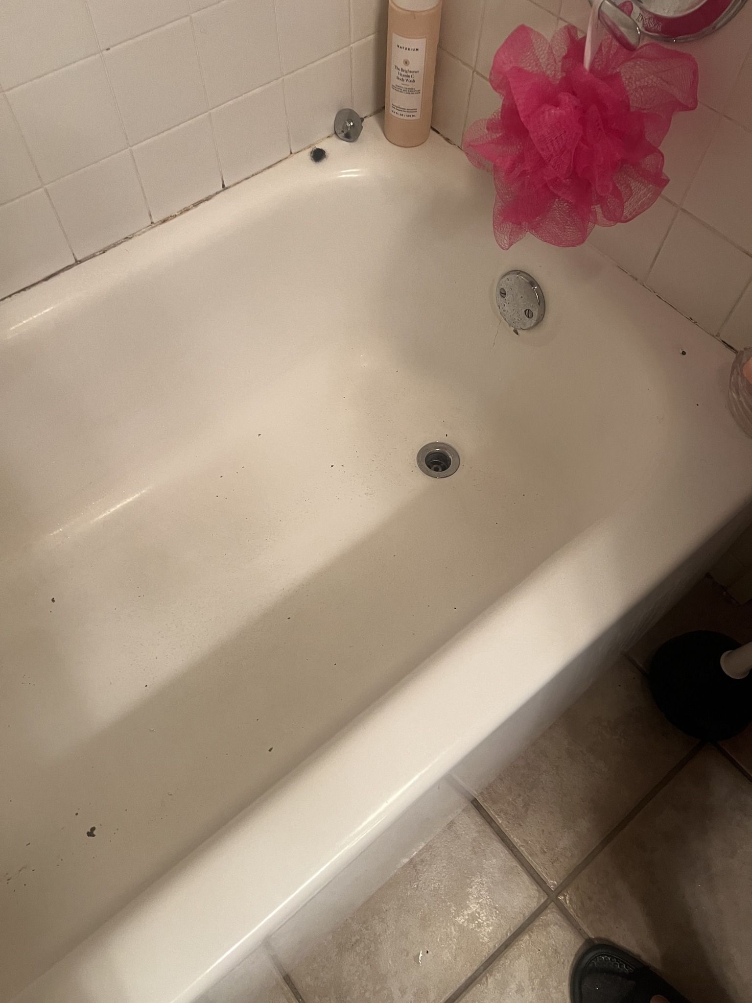 A white bathtub in a bathroom with a pink shower sponge.