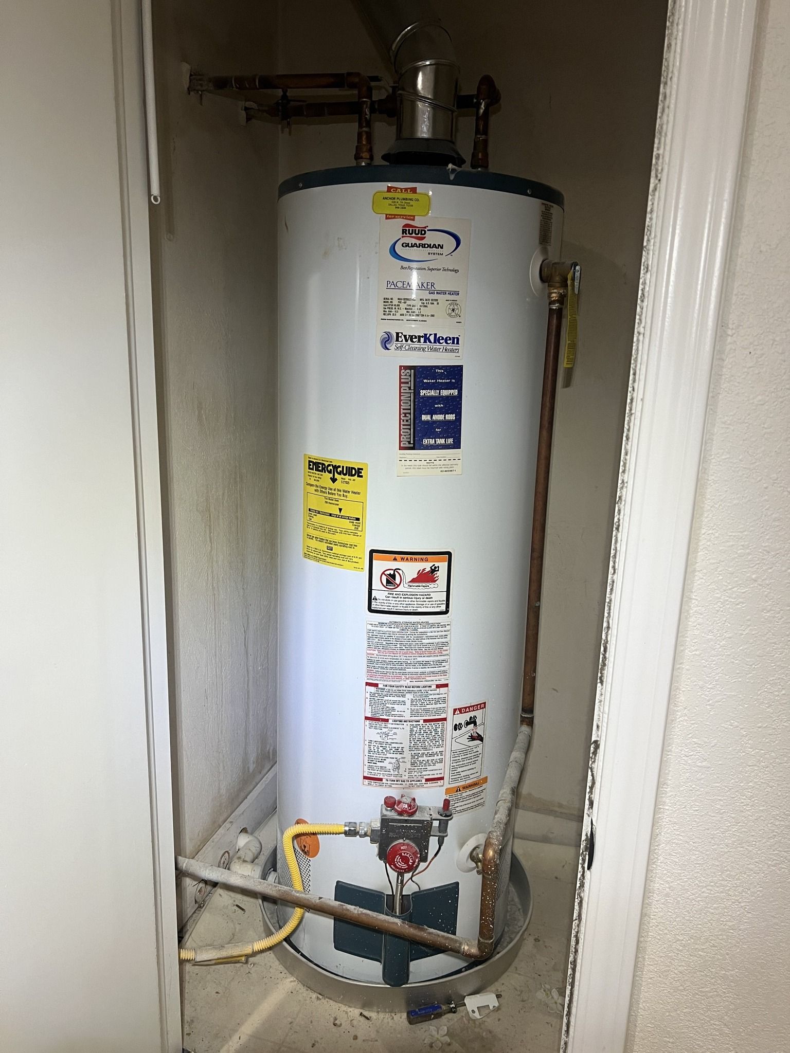 A water heater is sitting in a corner of a room next to a door.