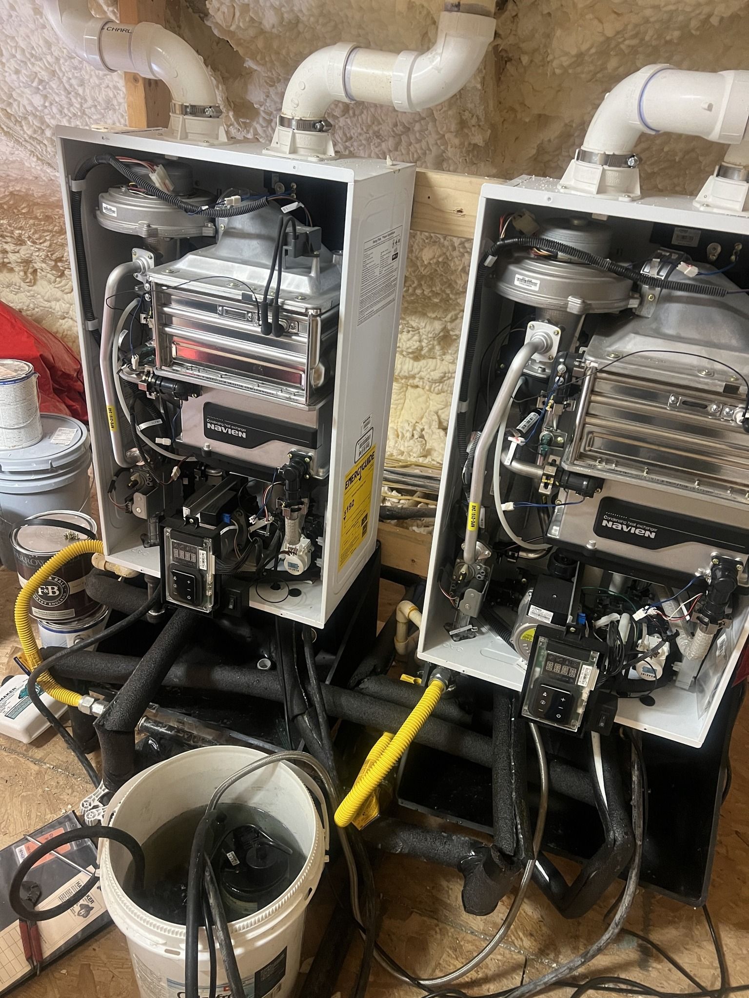 Two boilers are sitting next to each other in a basement.