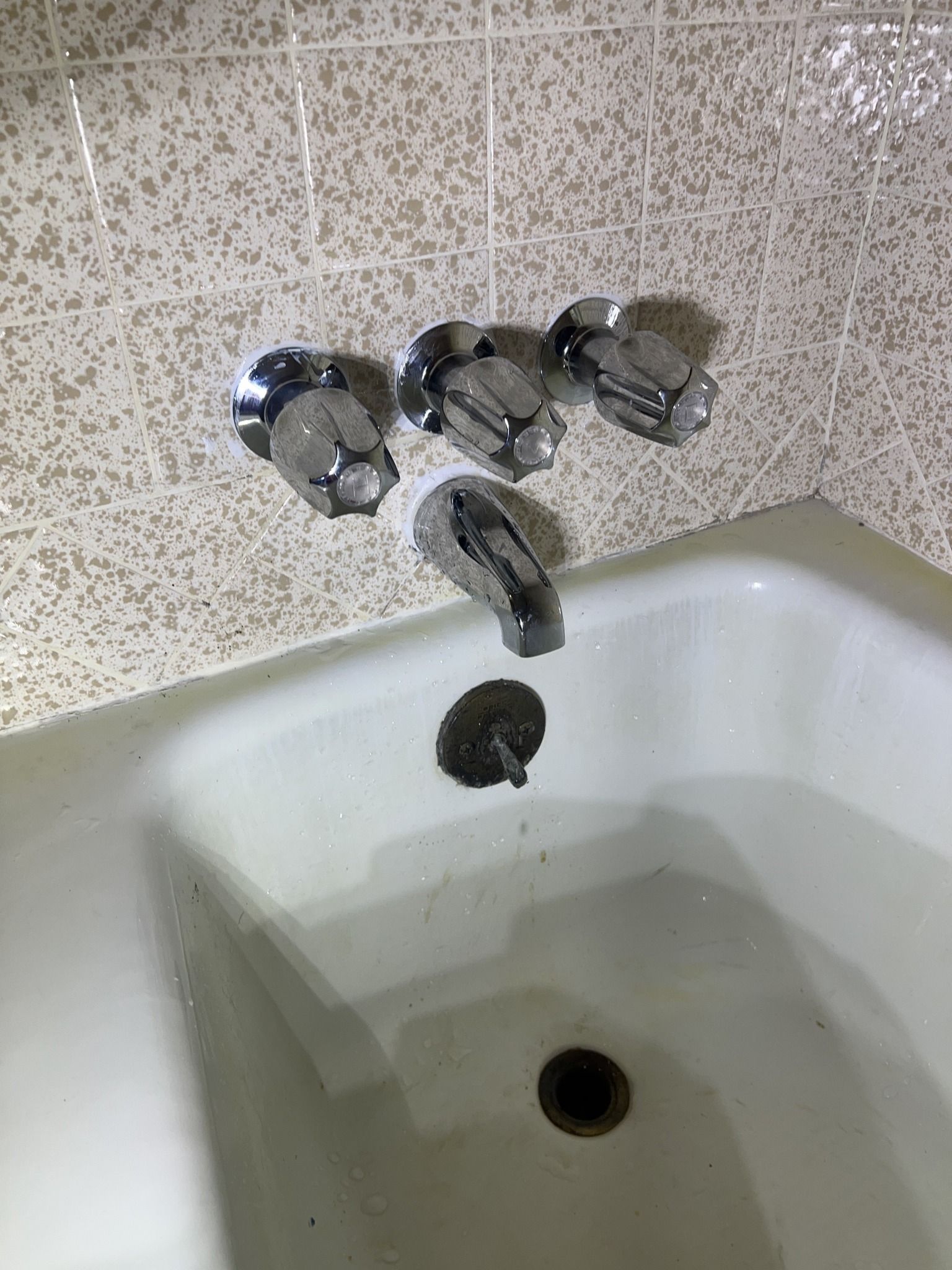 A bathtub with three faucets and a drain in a bathroom.