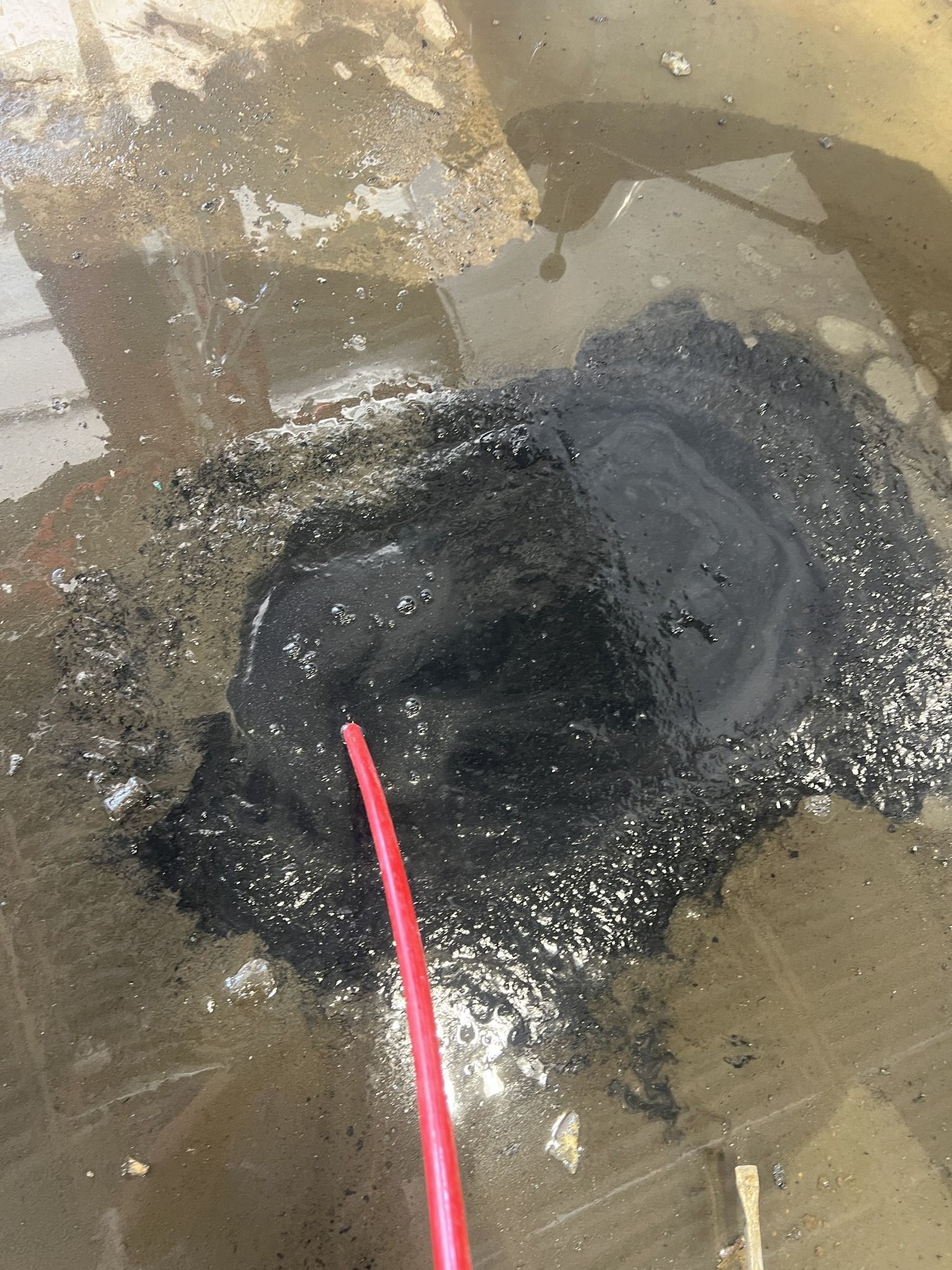 A red hose is sticking out of a hole in the ground.