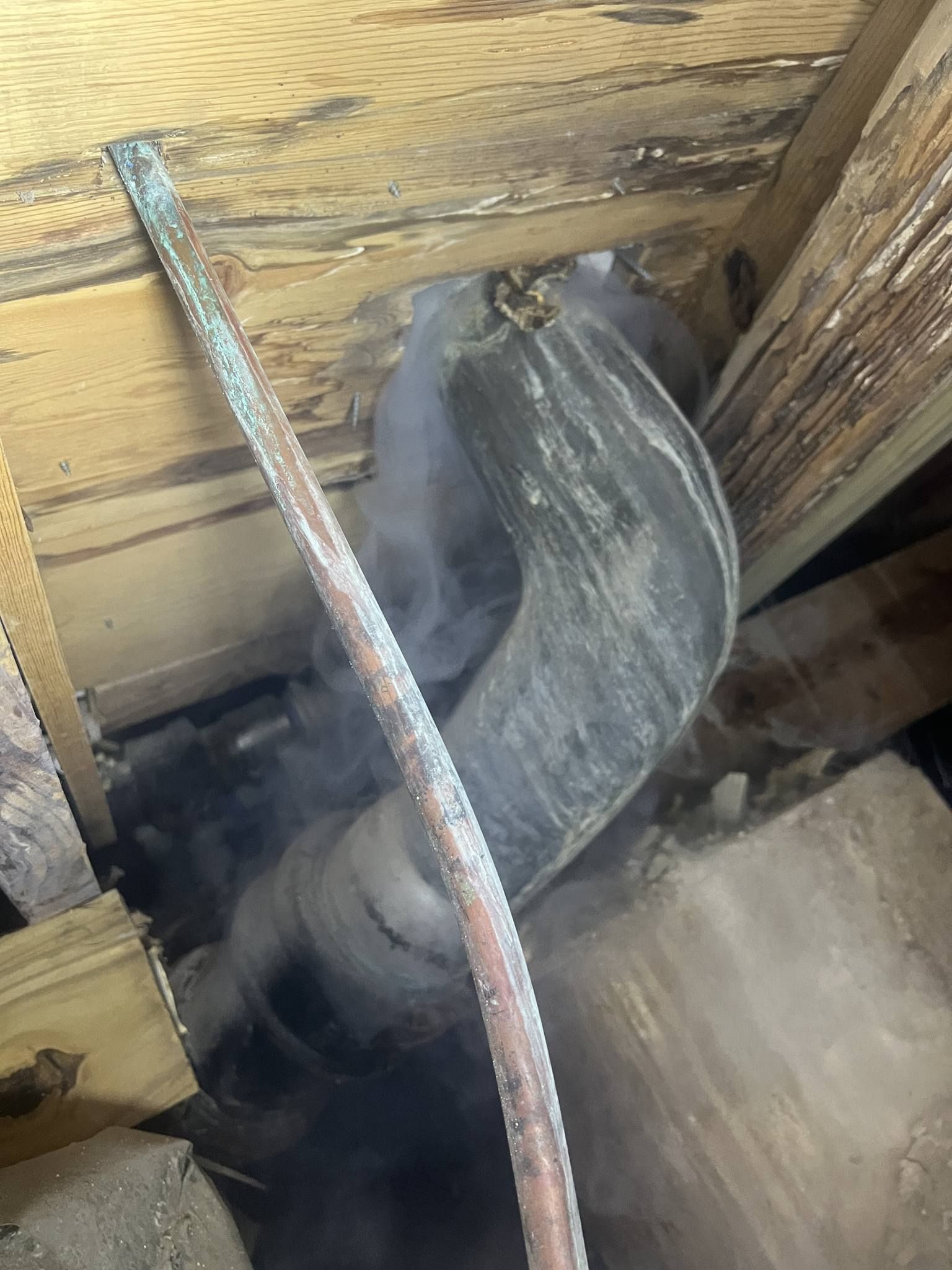 A person is cutting a pipe with a saw in a wooden room.