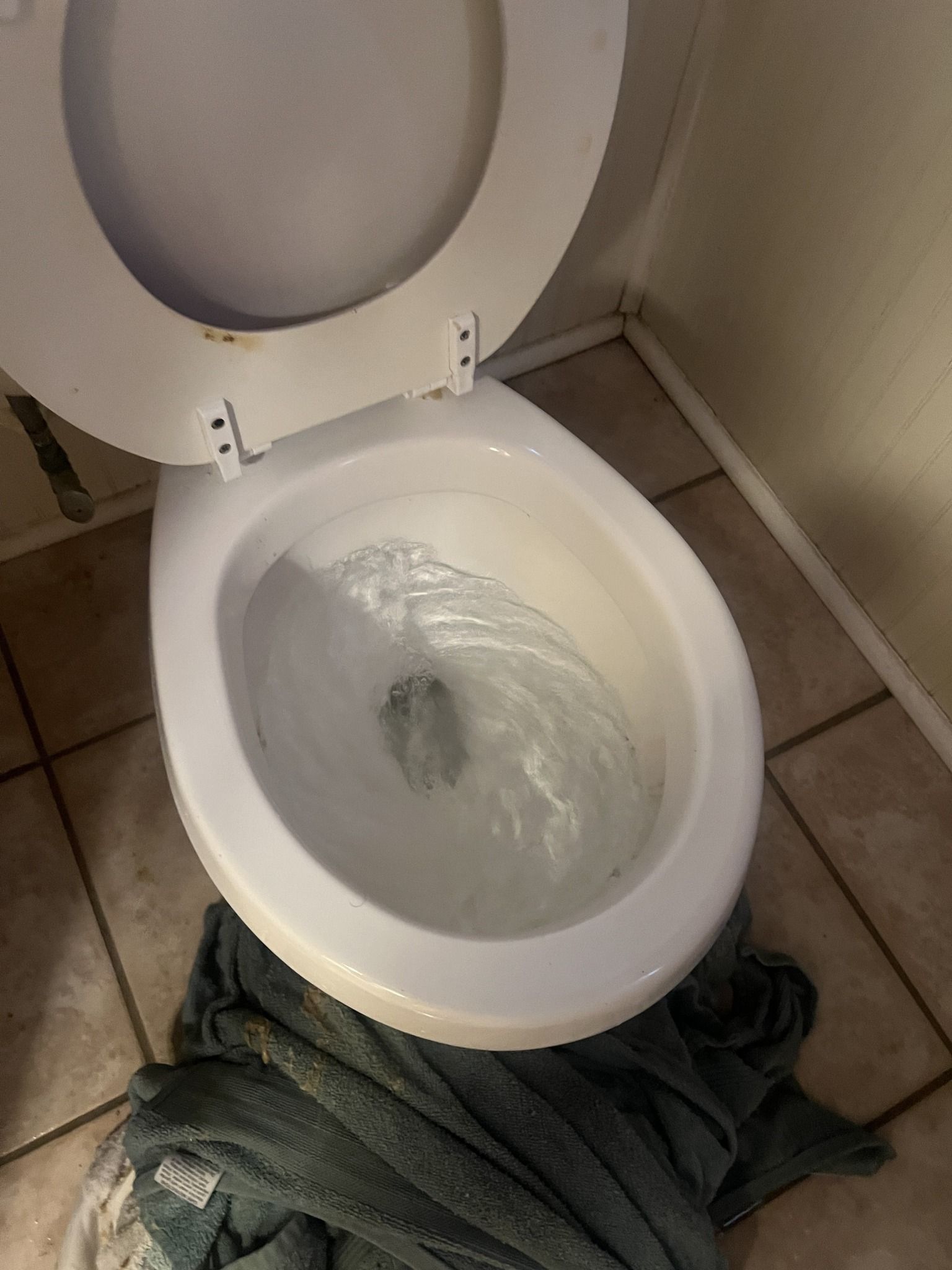 A toilet is sitting on a tiled floor next to a towel.
