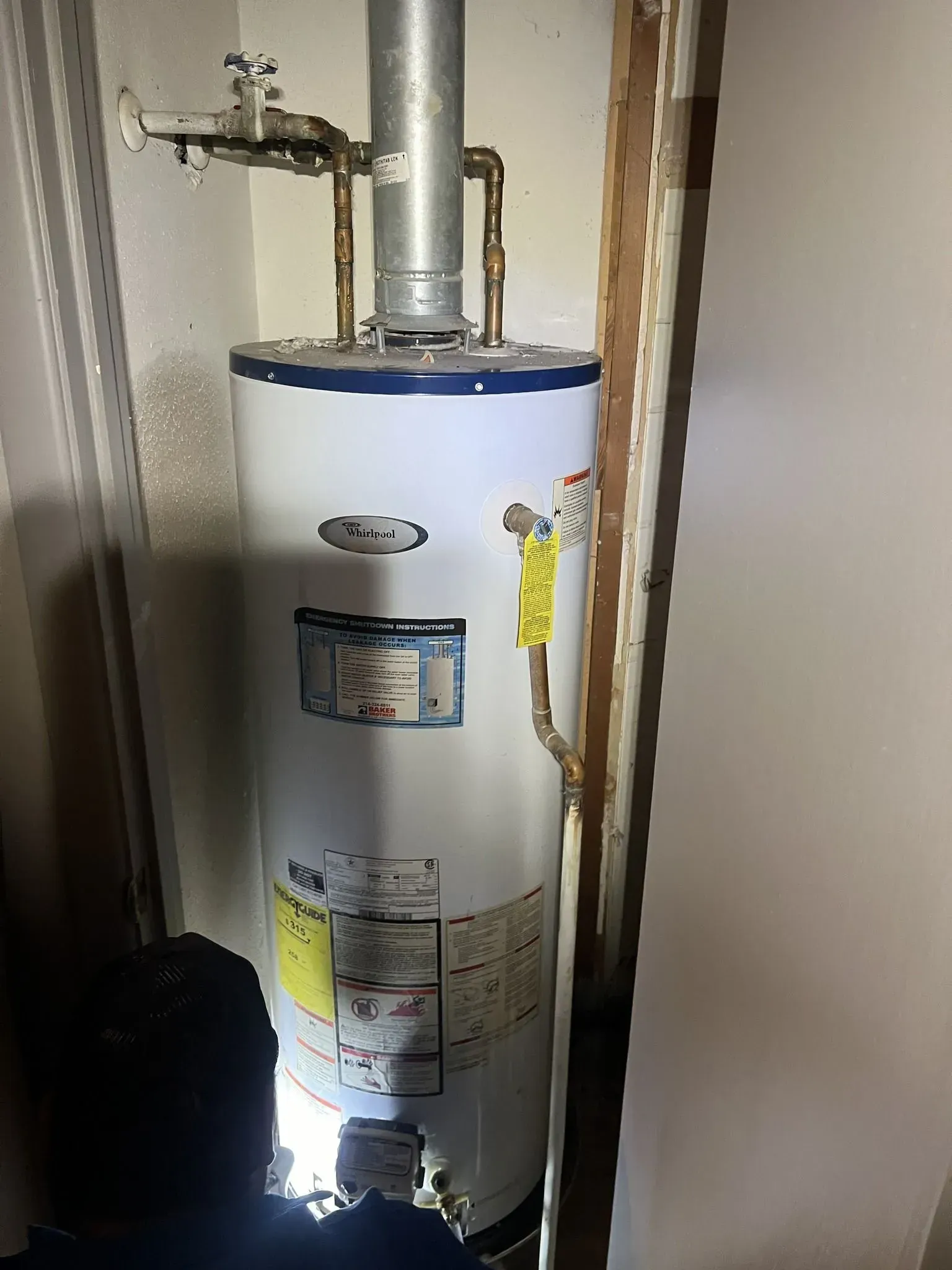 A white water heater is sitting in a corner of a room.