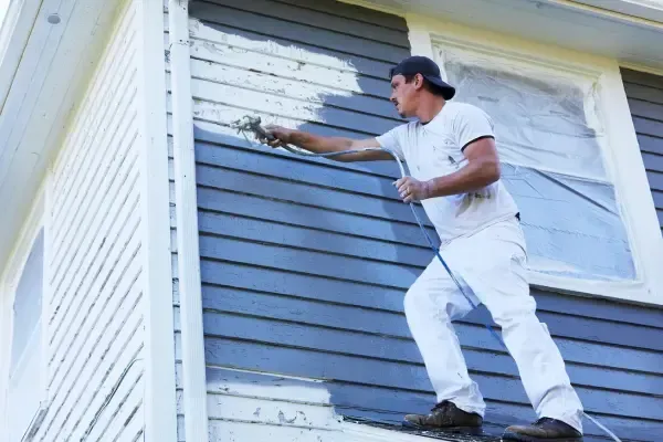 A Honolulu house painter is painting the side of a house with a sprayer.