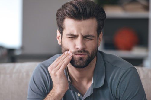 man with tooth pain holding jaw, what is TMJ blog