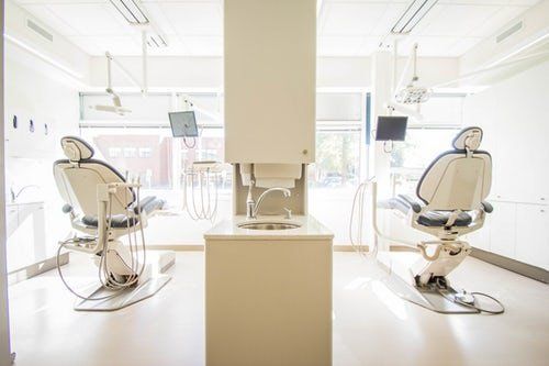 two-dental-chairs-facing-windows-separated-by-white-wall-with-sink