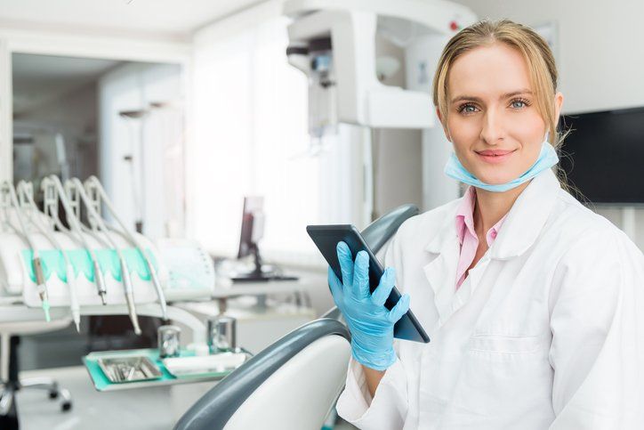 female-dentist-smiling-in-dental-office-while-holding-tablet