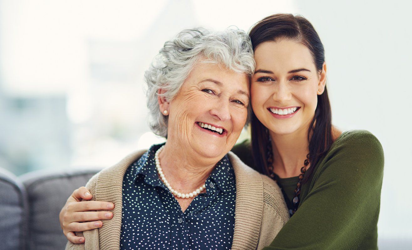 elderly-woman-and-adult-daughter-embracing-while-smiling-at-camera