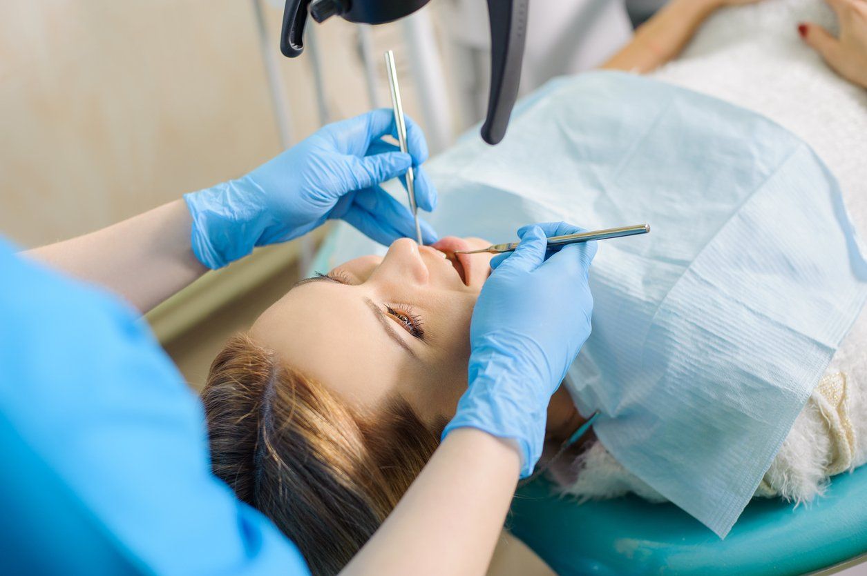 woman-being-examined-by-dentist-with-blue-gloves-and-dental-instruments