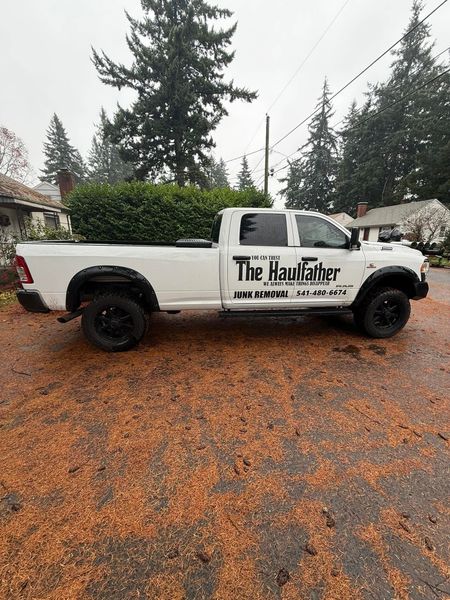 White pickup truck with “The Paint Guy” logo parked on a wet, leaf-covered driveway in front of evergreens