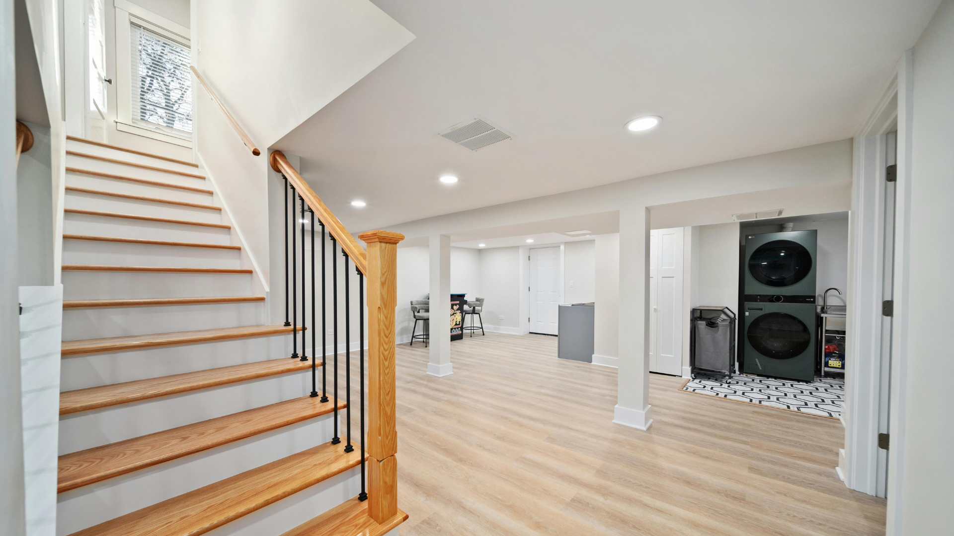 Basement with staircase, laundry machines, and open space with light wood floors.