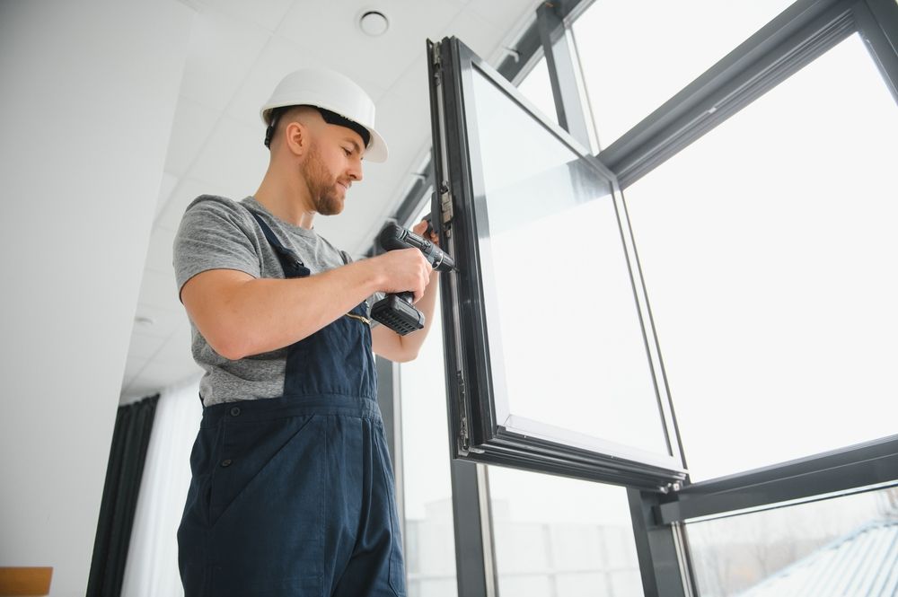 Man in overalls and hard hat sealing a window with a caulk gun.