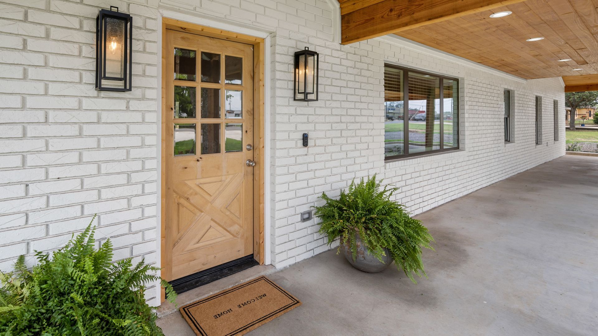 Whitewashed brick exterior with wooden door, ferns, and porch; modern farmhouse style.
