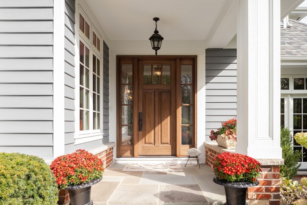 Wooden front door with sidelights, porch, planters, and hanging lantern.