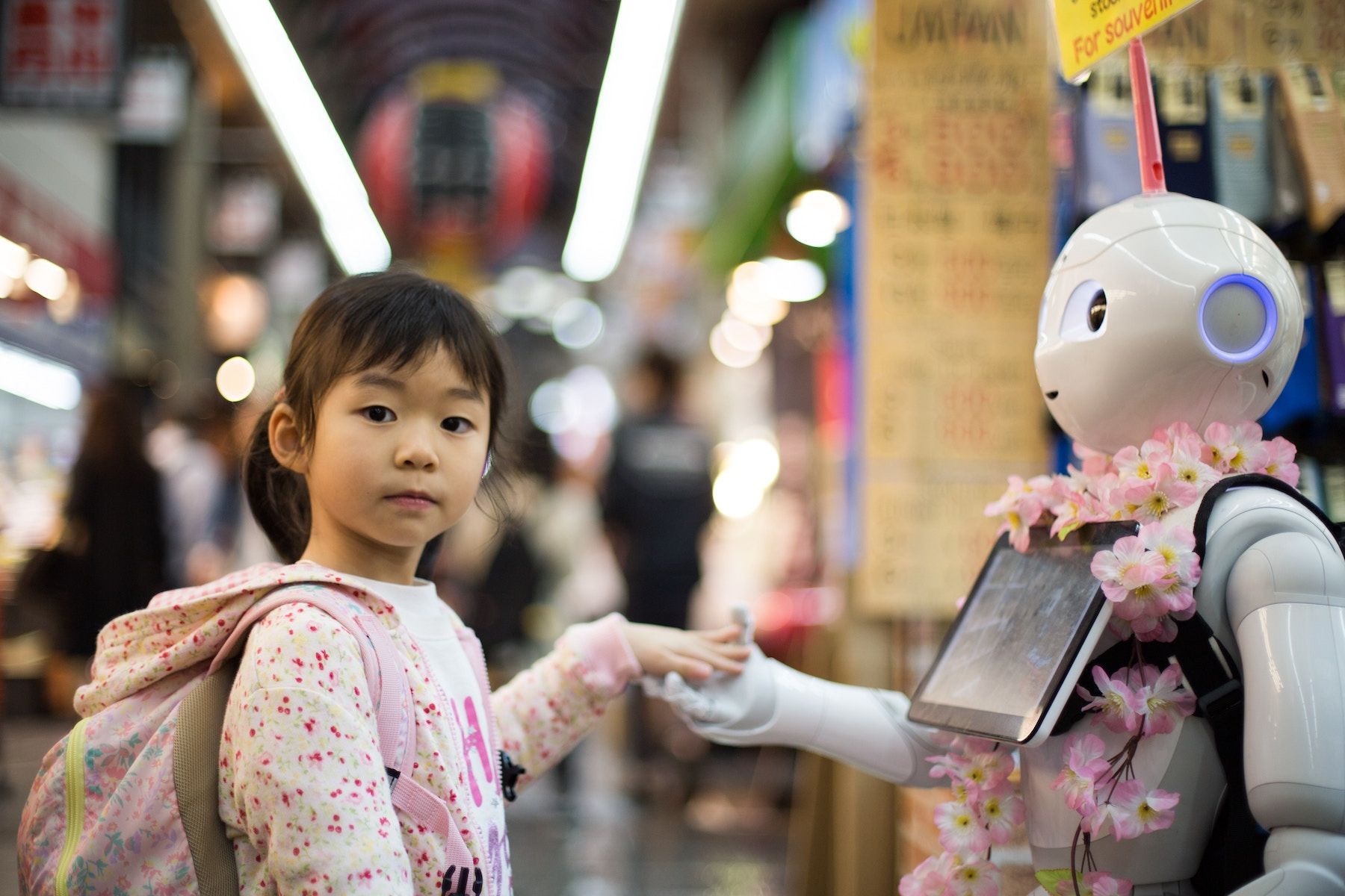 a little girl shakes hands with a robot that has flowers on it