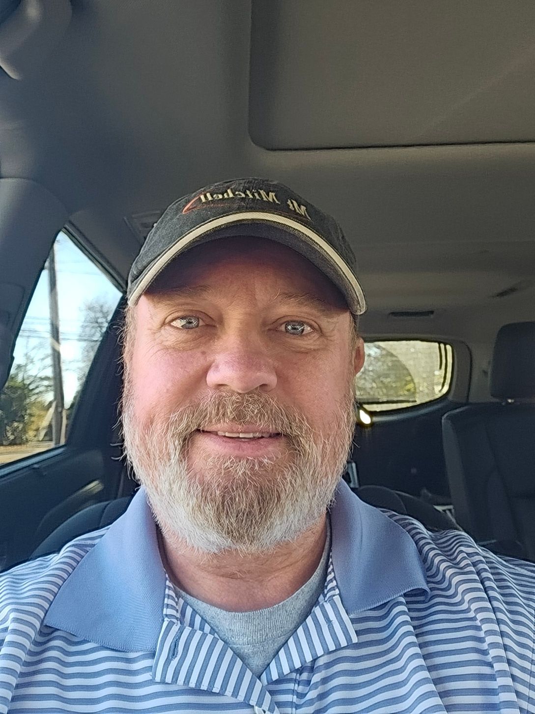 A man with a beard and hat is sitting in a car.