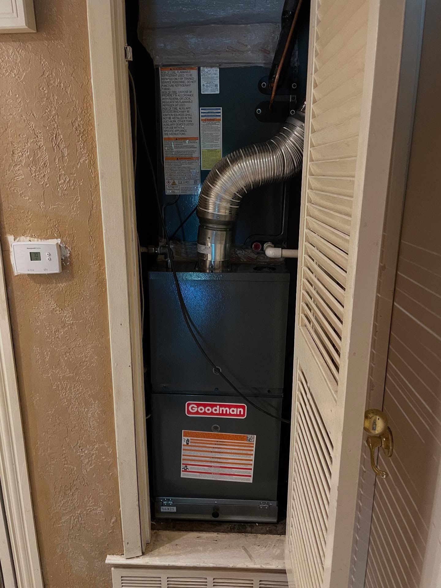 A Goodman furnace inside a closet with louvered doors.