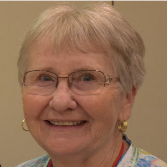 A woman wearing glasses and earrings smiles for the camera