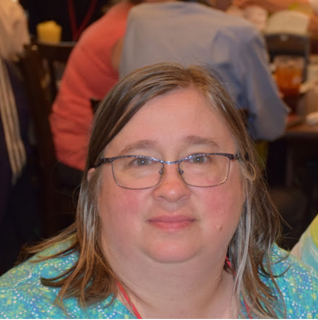 A woman wearing glasses is sitting at a table with other people