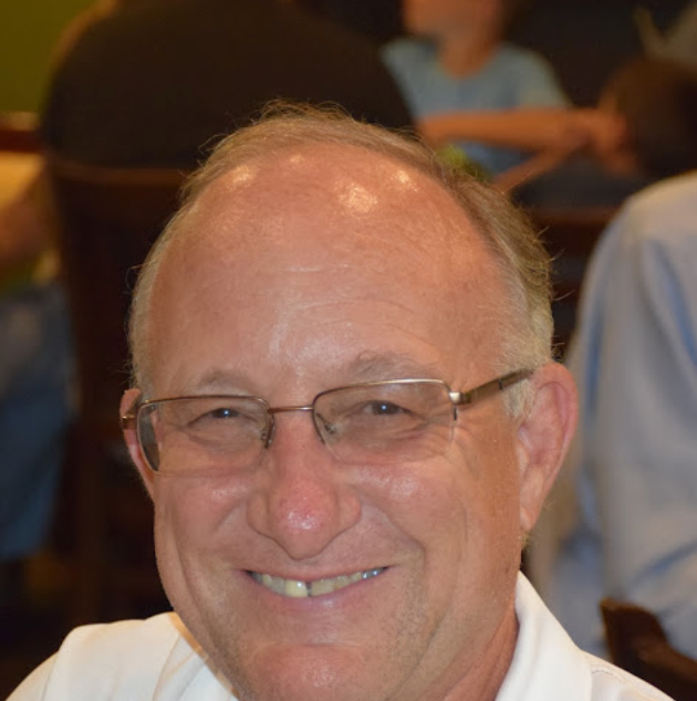 A man wearing glasses and a white shirt smiles for the camera