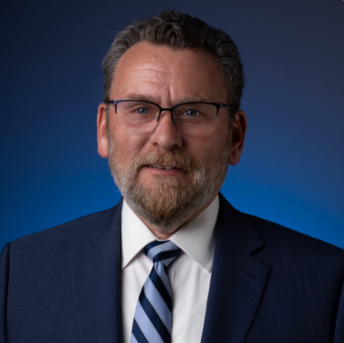 A man with glasses and a beard is wearing a suit and tie