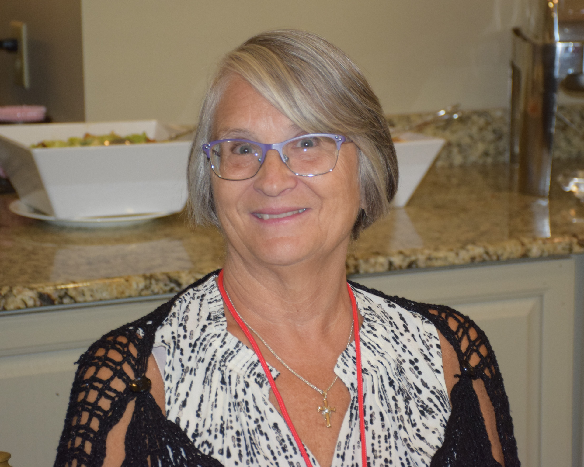 A woman wearing glasses and a lanyard is sitting at a counter.