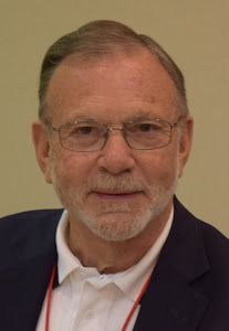 A man with a beard and glasses is wearing a suit and a white shirt.