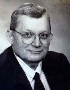 A black and white photo of a man wearing glasses and a suit and tie.