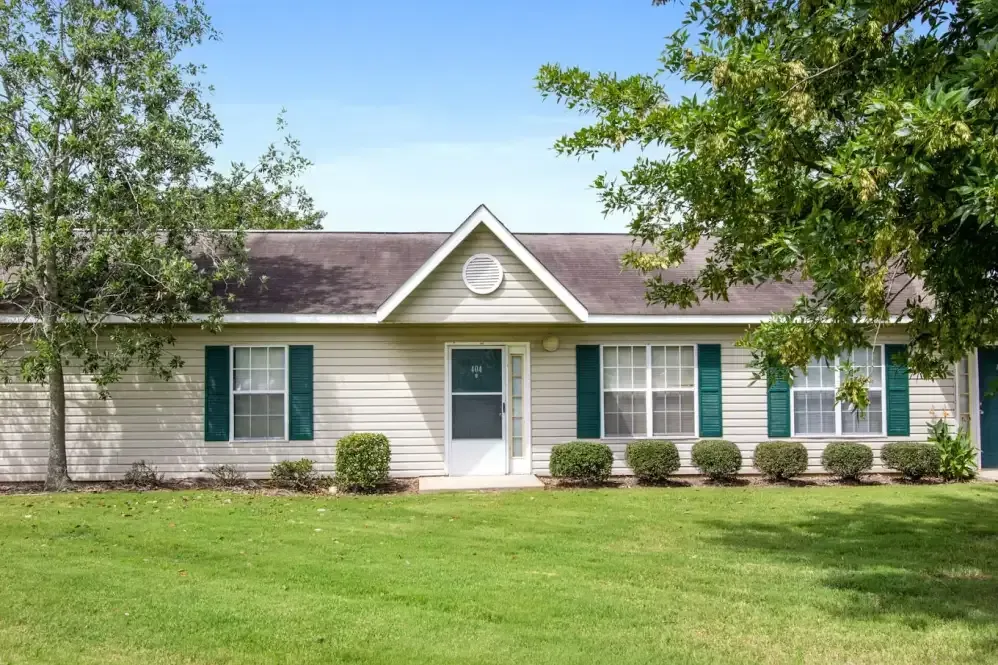 Tan ranch house with green shutters and a front lawn under a blue sky.