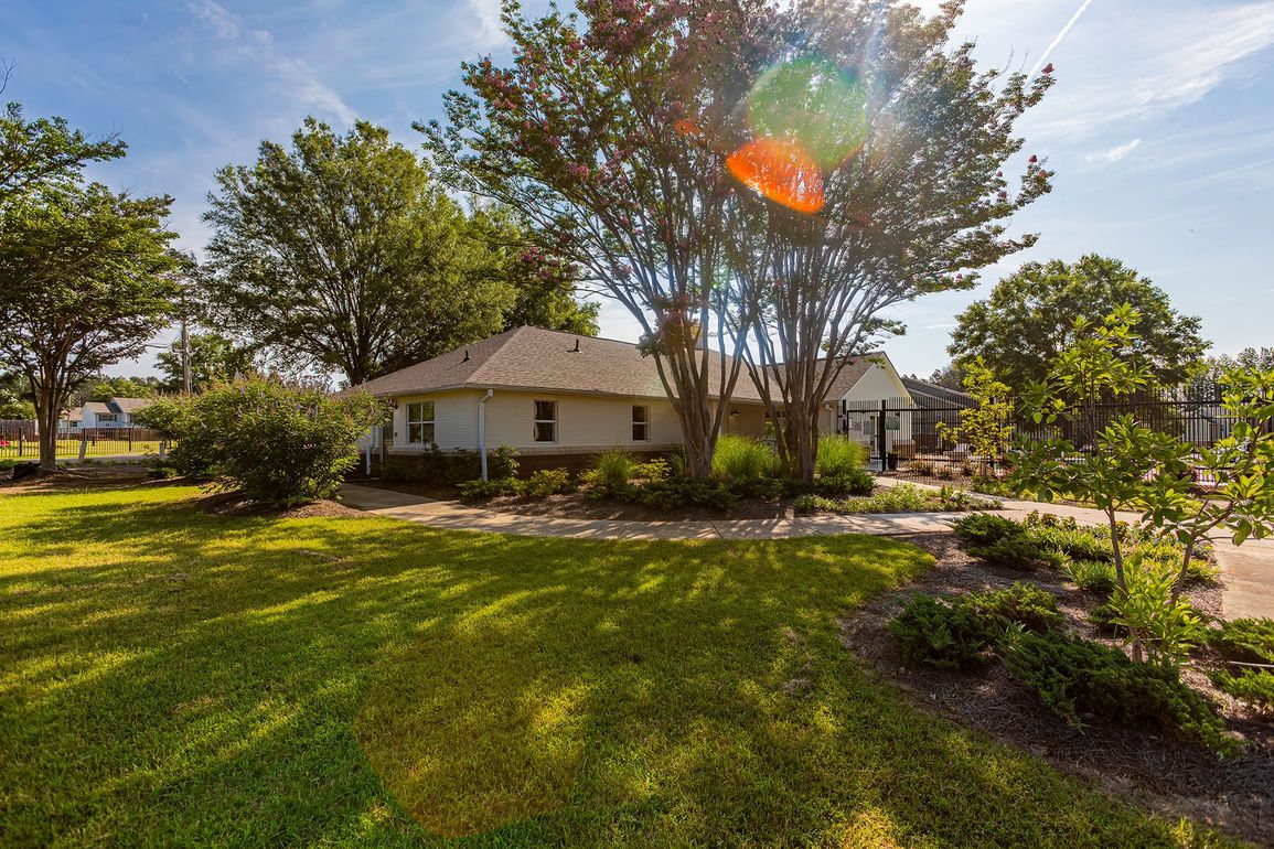 A one-story house with a green lawn and trees under a bright blue sky.